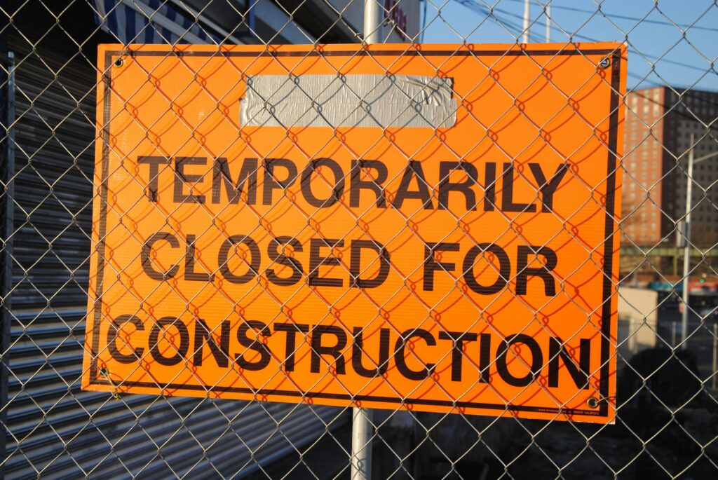 Orange sign behind fence reading 'Temporarily Closed for Construction' at site.