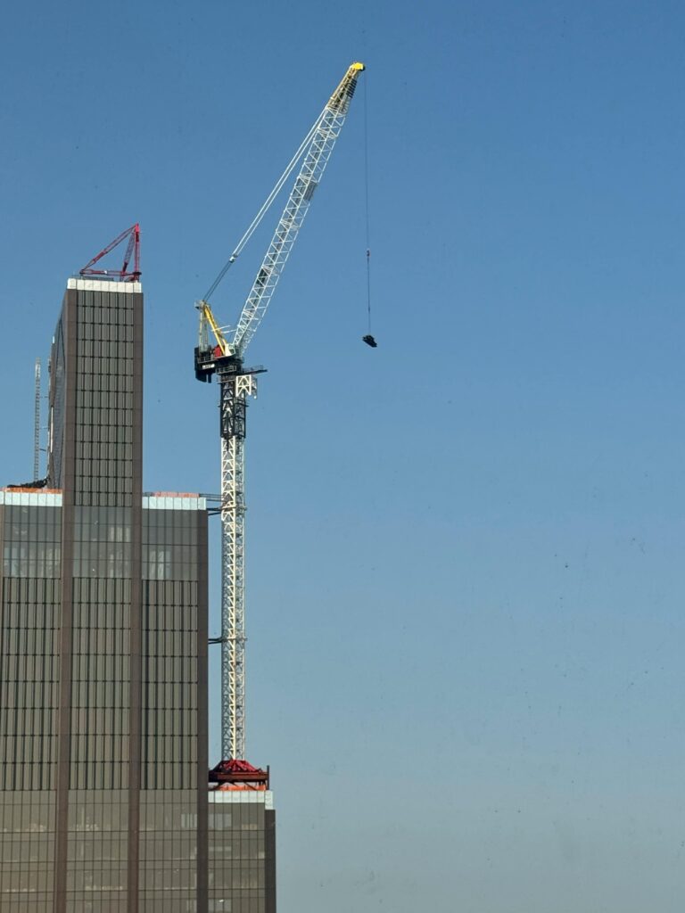 Tower crane operating on a high-rise building against a clear blue sky.