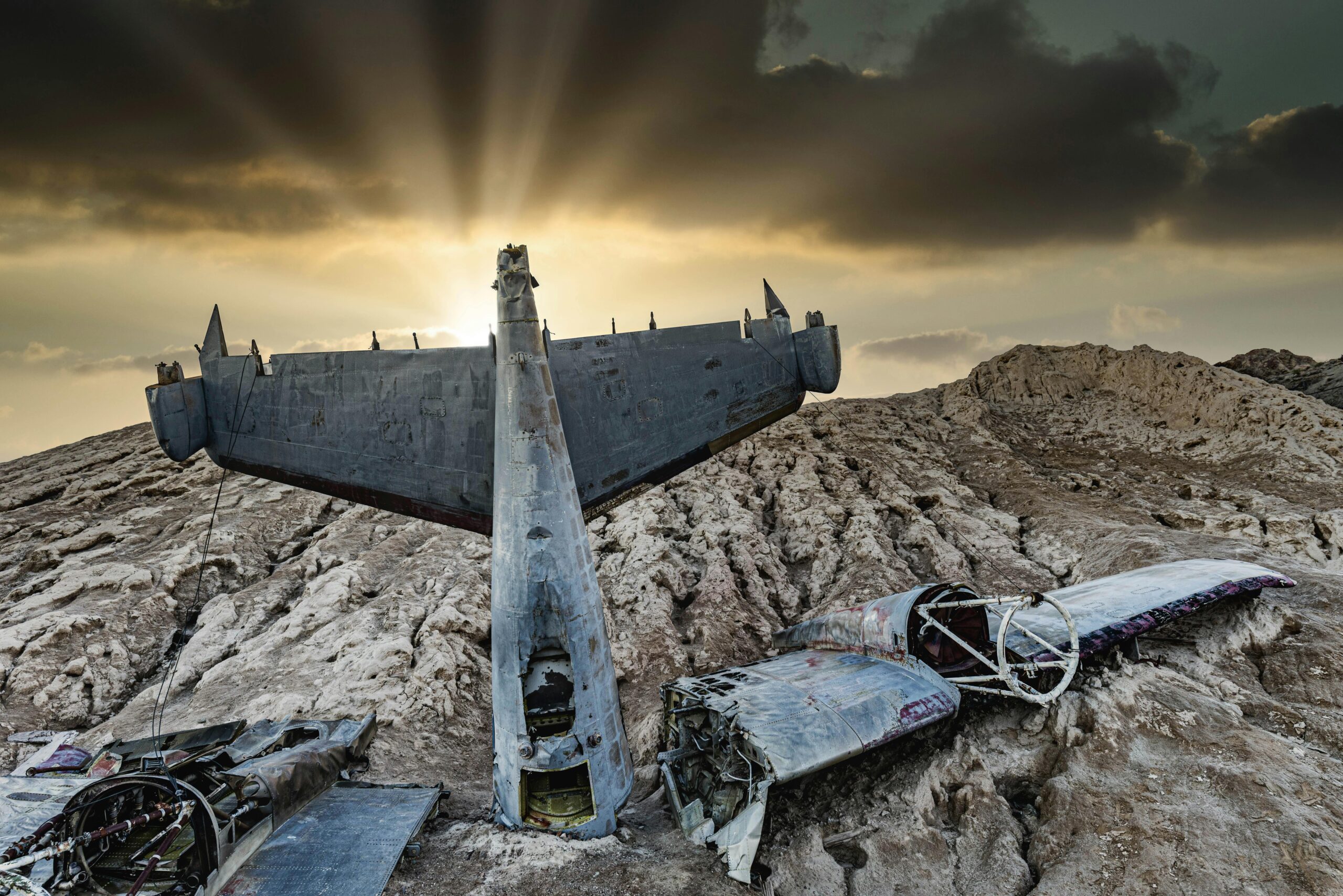 Dramatic sunset illuminating a crashed aircraft in a barren desert landscape.