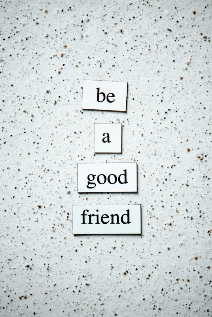 Text tiles 'be a good friend' on a pebbled surface for inspiring friendship.